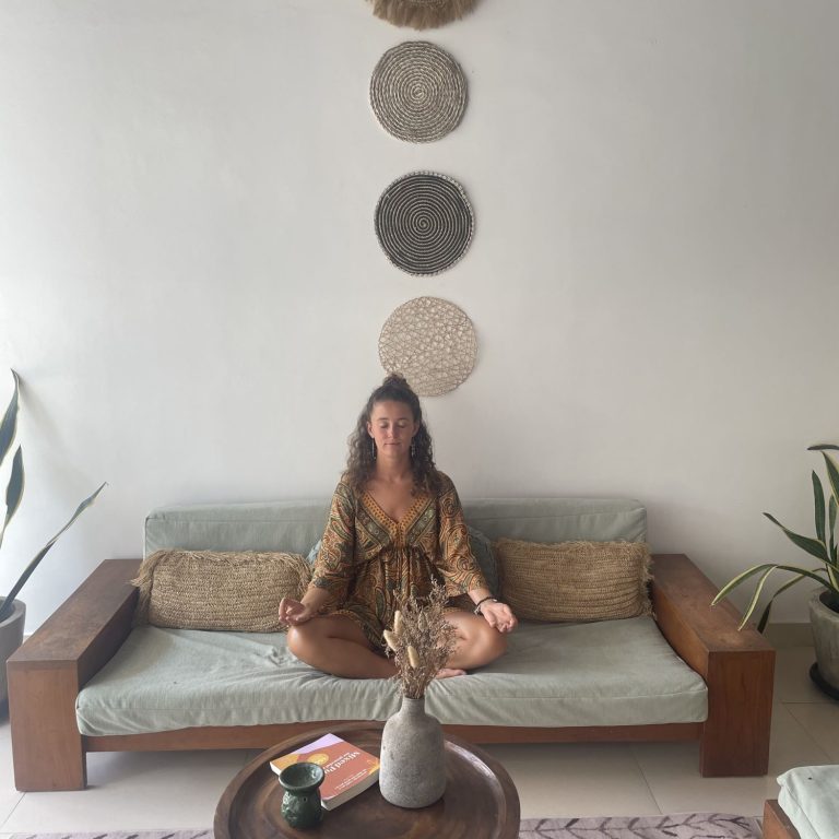 eine Frau sitzt in einer Yoga-Pose im Schneidersitz auf einer Bank und hat die Augen geschlossen