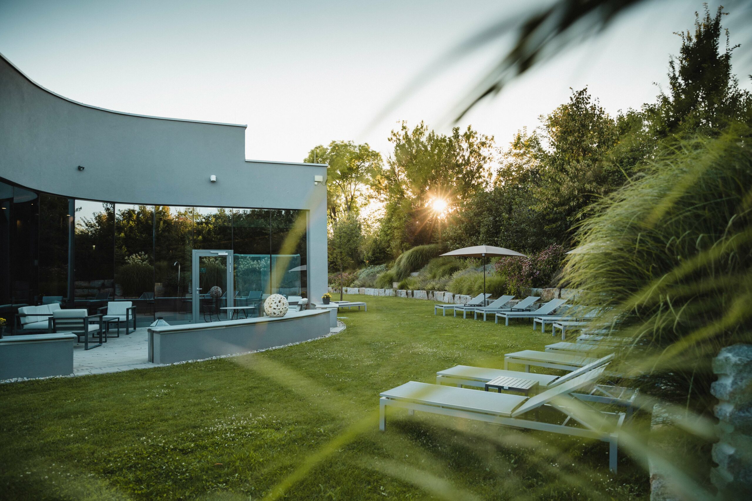 Garten Eden im Silent Spa mit viel grün, Einzelliegen und Sonnenschirm. Die Sonne geht langsam unter.
