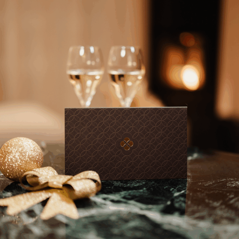Am Tisch ist ein Gutschein platziert mit weihnachtlicher Deko und 2 Sektgläsern