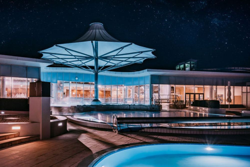 Nachtaufnahme vom Außenbereich in die beleuchtete Therme 